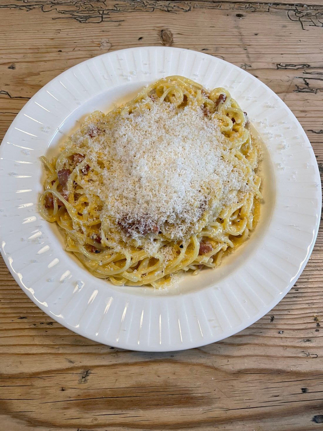 A huge portion of spaghetti carbonara in a white dinner bowl with finely grated parmesan on top