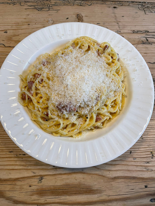 A huge portion of spaghetti carbonara in a white dinner bowl with finely grated parmesan on top